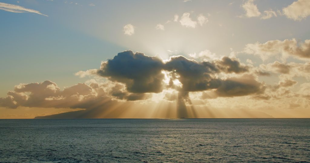 Bright sun light ray, sunbeam shining through colorful dark cumulus cloud. Pastel blue sky in